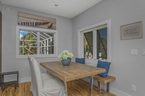 Un coin repas avec une table en bois, des chaises à revêtement blanc et un coussin bleu.