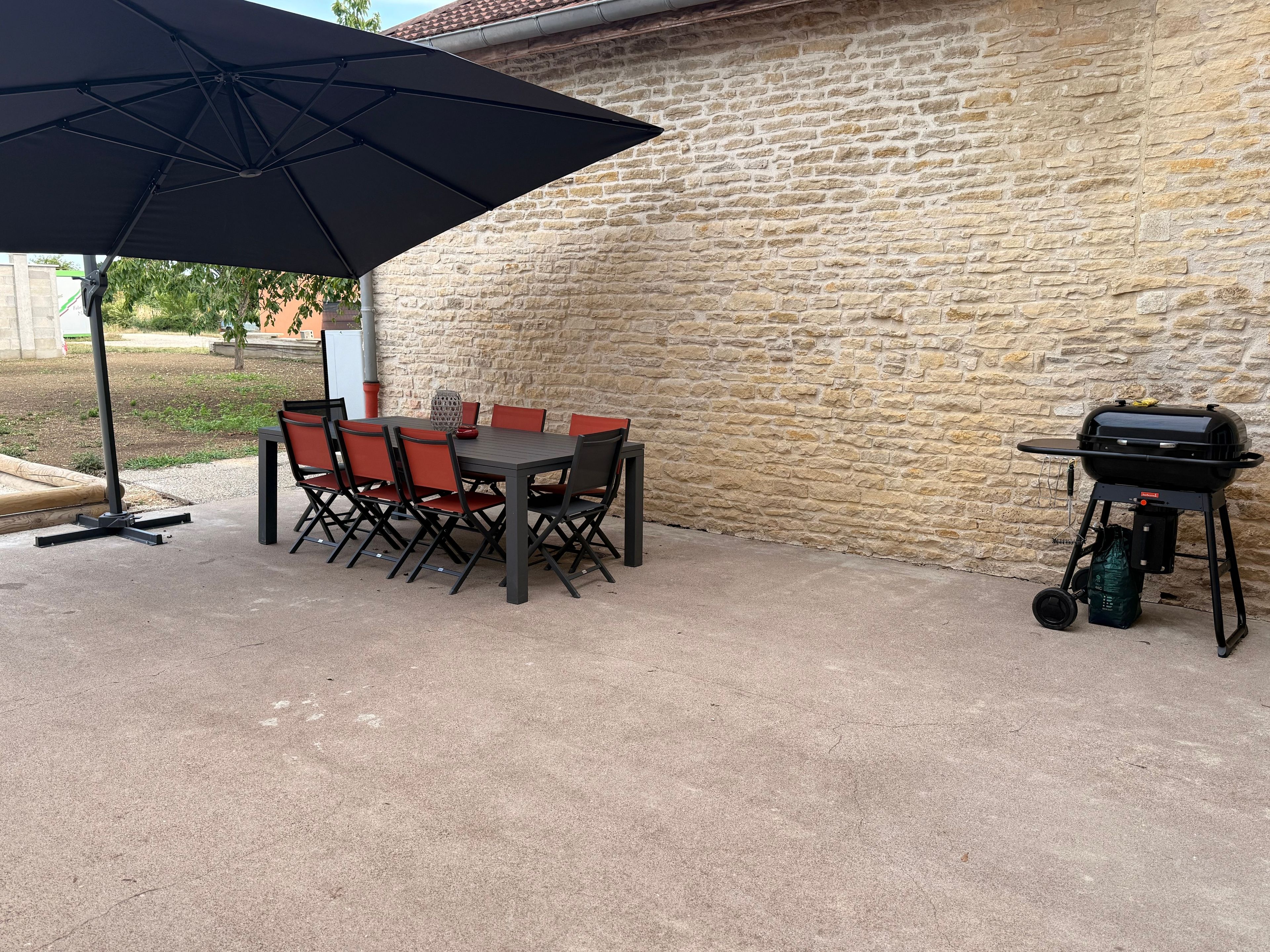 Une terrasse extérieure avec une table et des chaises, un barbecue et un grand parasol.