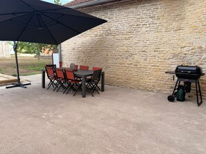 Een terras buiten met een tafel, stoelen, een barbecue en een grote parasol.