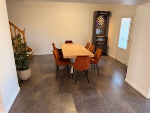 A dining area with a wooden table and orange chairs, a dartboard, and a potted plant. - Holiday Home 'Player One Comfortable House' with Private Terrace, Private Garden and Wi-Fi (Villiers-le-Sec)