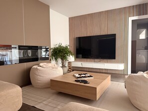 Een moderne woonkamer met een houten salontafel, een grote flatscreen televisie aan de muur en een pot met een plant.