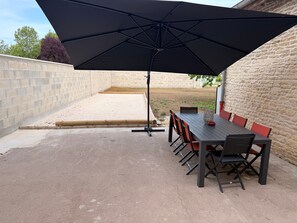 An outdoor patio with a table and chairs, a large umbrella, and a brick wall. - Holiday Home 'Player One Comfortable House' with Private Terrace, Private Garden and Wi-Fi (Villiers-le-Sec)