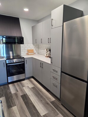 A modern kitchen with stainless steel appliances, grey cabinetry, and a herringbone-patterned wood floor. - The Upper Haven - Cozy rural suite (Saint Brieux)