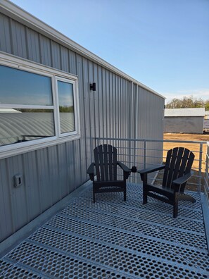 A metal building with a window and a metal deck with a table and two chairs. - The Upper Haven - Cozy rural suite (Saint Brieux)