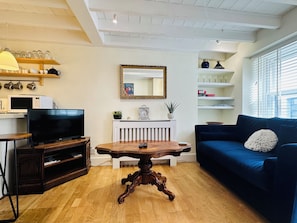 Een woonkamer met een donkerblauwe bank, een houten salontafel, een televisie en een witte radiator.