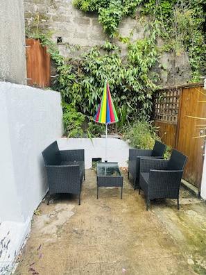 Een terras met rieten meubilair en een felgekleurde parasol.