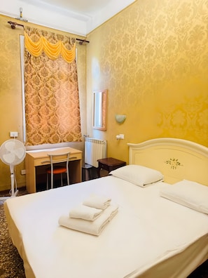 Ein Hotelzimmer mit Bett, Schreibtisch, Stuhl, Spiegel, Heizkörper und einer Wandleuchte.