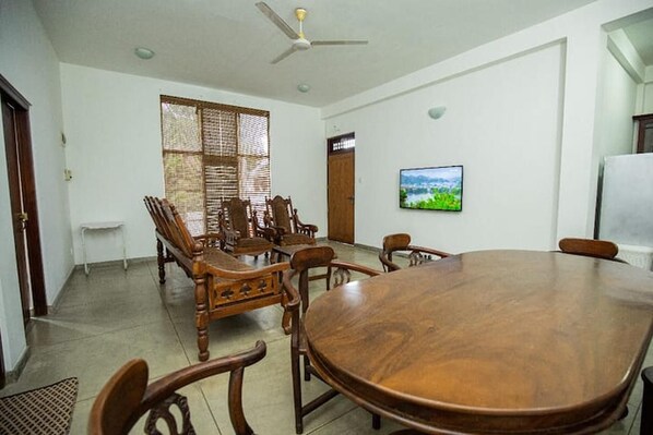 A conference room with a large wooden table, several chairs, a ceiling fan, and a television on the wall.