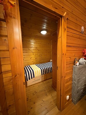 L’intérieur d’un chalet en bois comprend un lit, une cheminée et une porte qui donne sur une autre pièce.