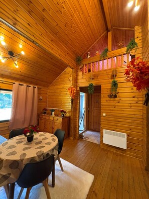 Un intérieur de chalet chaleureux avec un coin repas, un escalier et une vue sur l’extérieur.