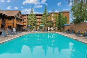 A swimming pool with lounge chairs and umbrellas, surrounded by multi-story buildings with balconies. - Chelan | Family Lake Retreat | Pool + Lake | 3BR Sleeps 8 (Chelan)