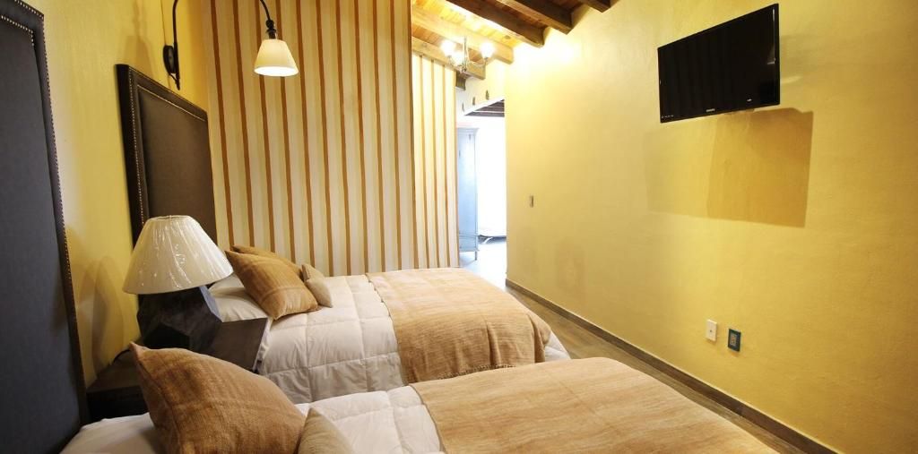 A hotel room with two beds, a lamp, a TV, and a striped wall.
