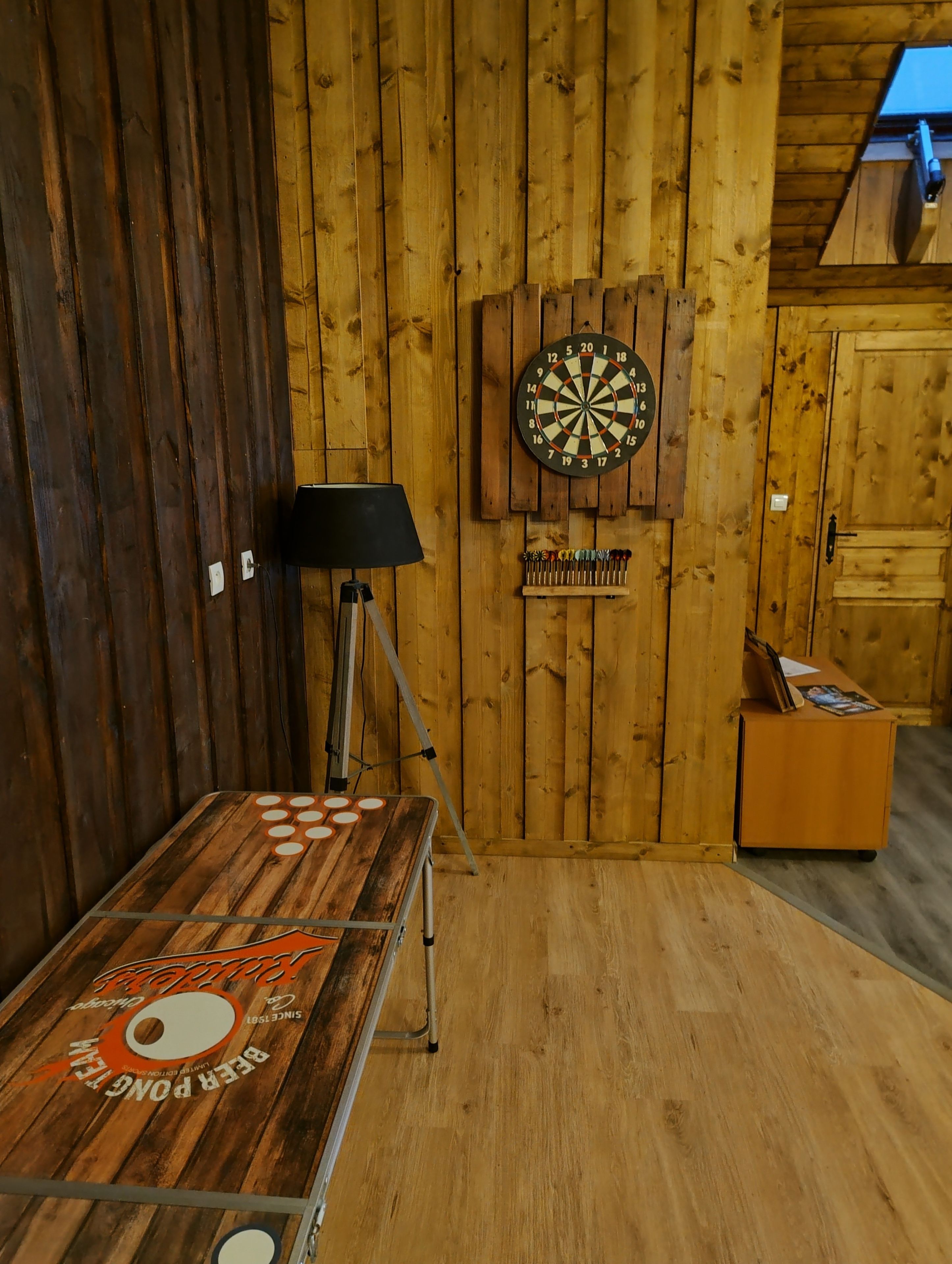 Een kamer met een dartbord, een tafel met een geruit patroon en een lamp.