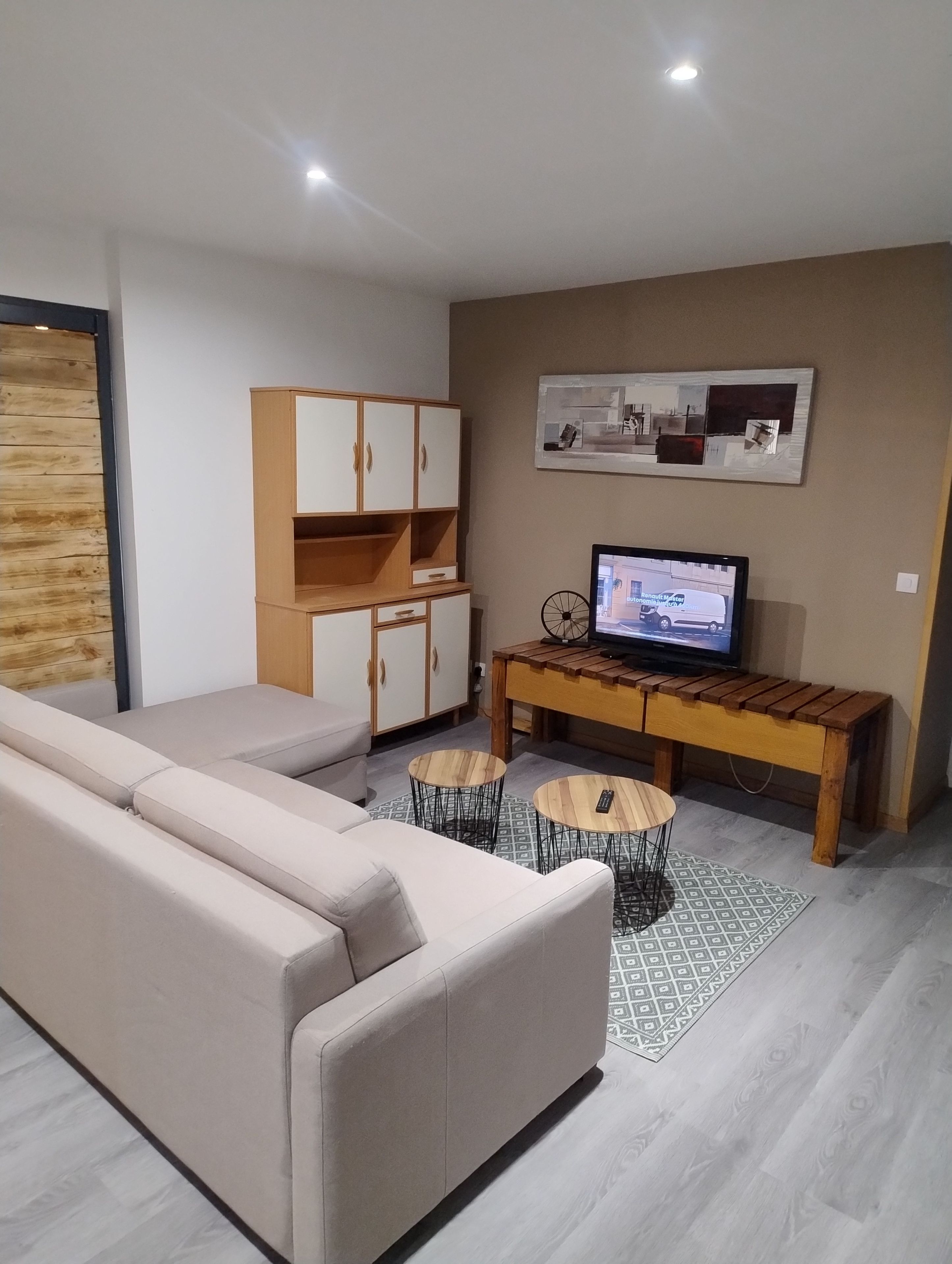 Een moderne woonkamer met een bank, een houten kast, een televisie en een klein rond tafeltje.