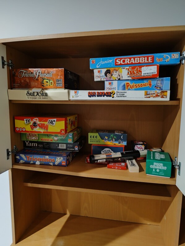 Un estante de madera con varios juegos de mesa, incluyendo Scrabble y Tic Tac Toe.