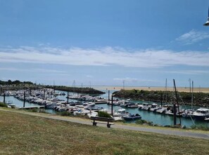 A marina with numerous boats docked, a sandy beach in the background, and a grassy area with a bench. - New Listing (Les Mathes)
