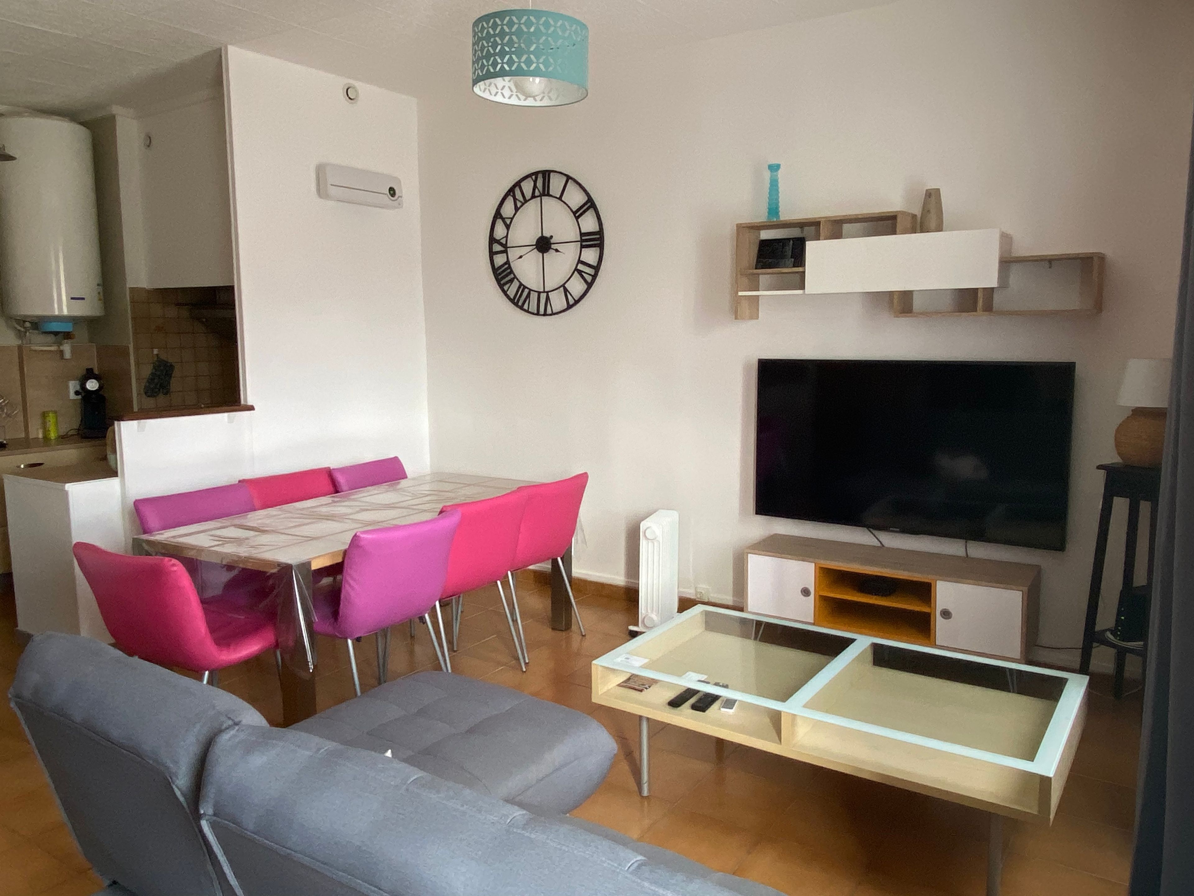 Un salon moderne avec un canapé, une table à manger et des chaises, un téléviseur et une horloge au mur.