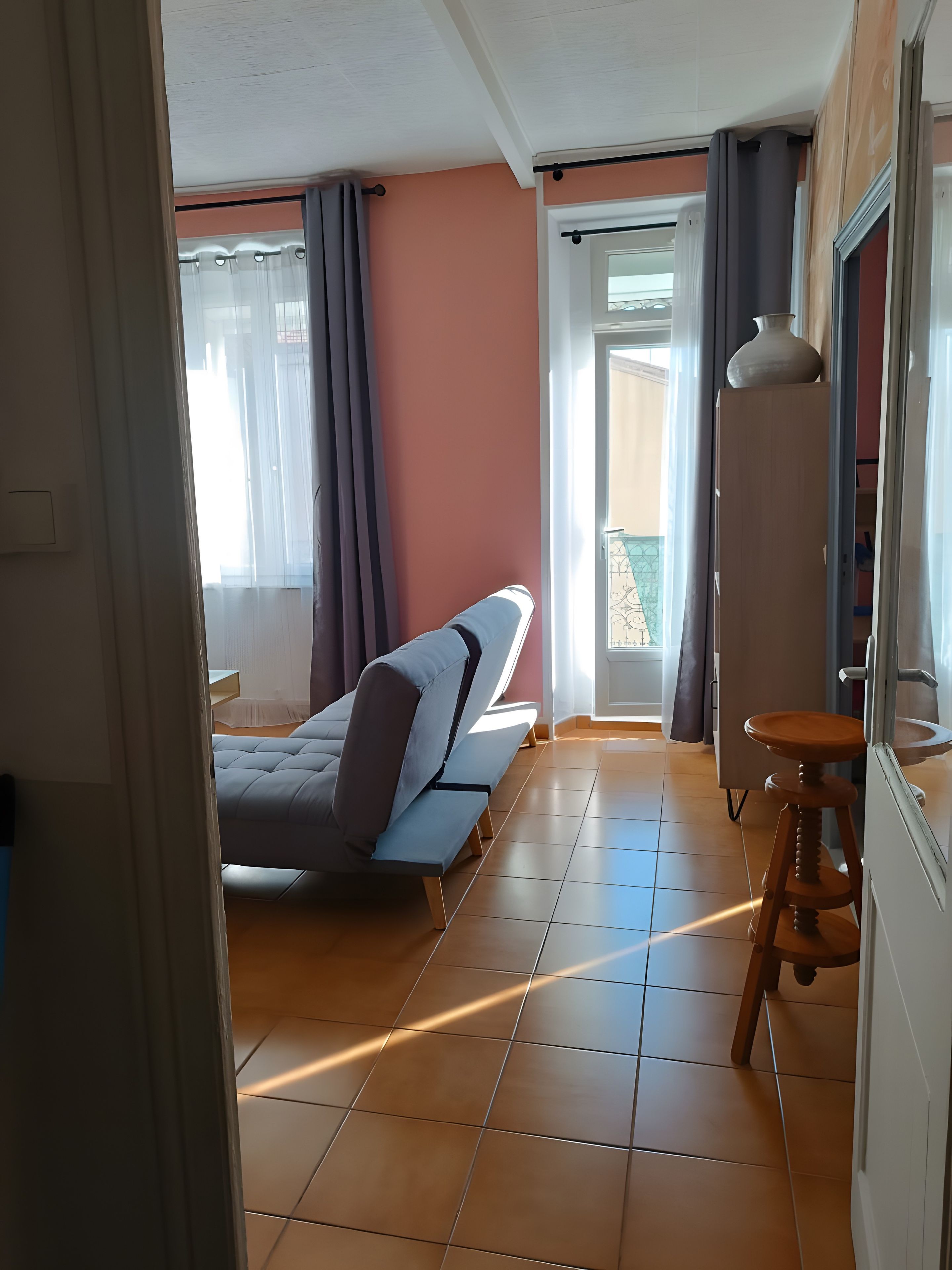 A room with a bed, a stool, and a window with curtains.