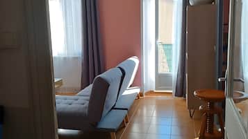 A room with a bed, a stool, and a window with curtains.