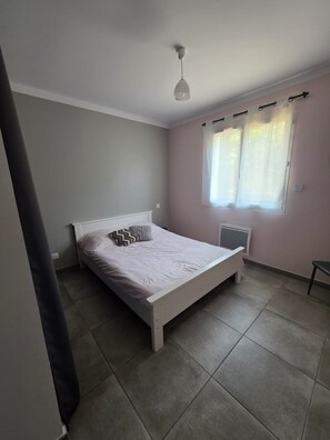 Un dormitori amb un llit individual, un radiador, una finestra amb cortines i una làmpada al sostre.
