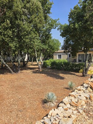 Zona exterior paisatjada amb arbres, una paret de roca i un edifici amb teulada enrajolada.