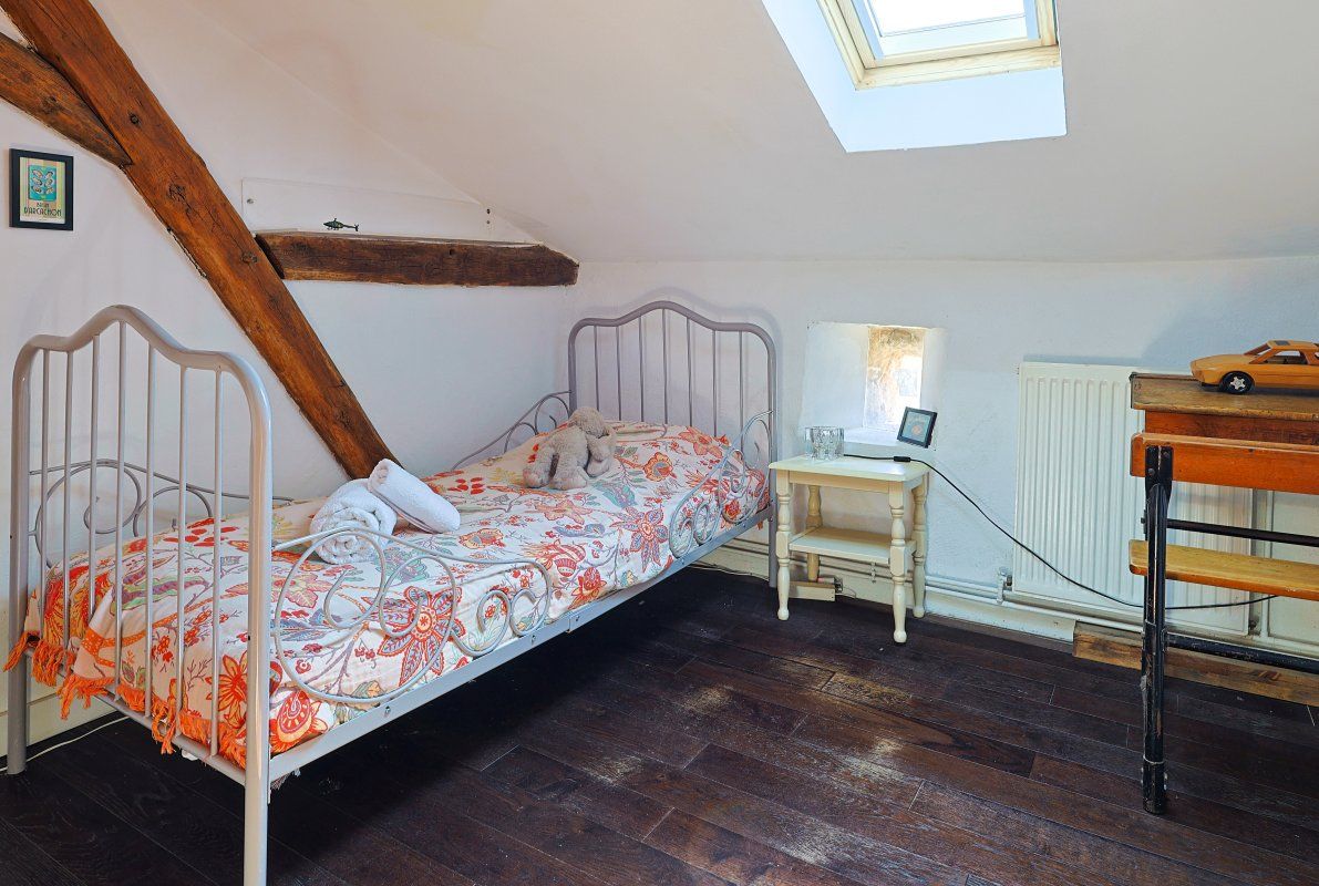 A bedroom with a sloped ceiling, a bed with a patterned bedspread, a desk with a lamp, and a radiator.