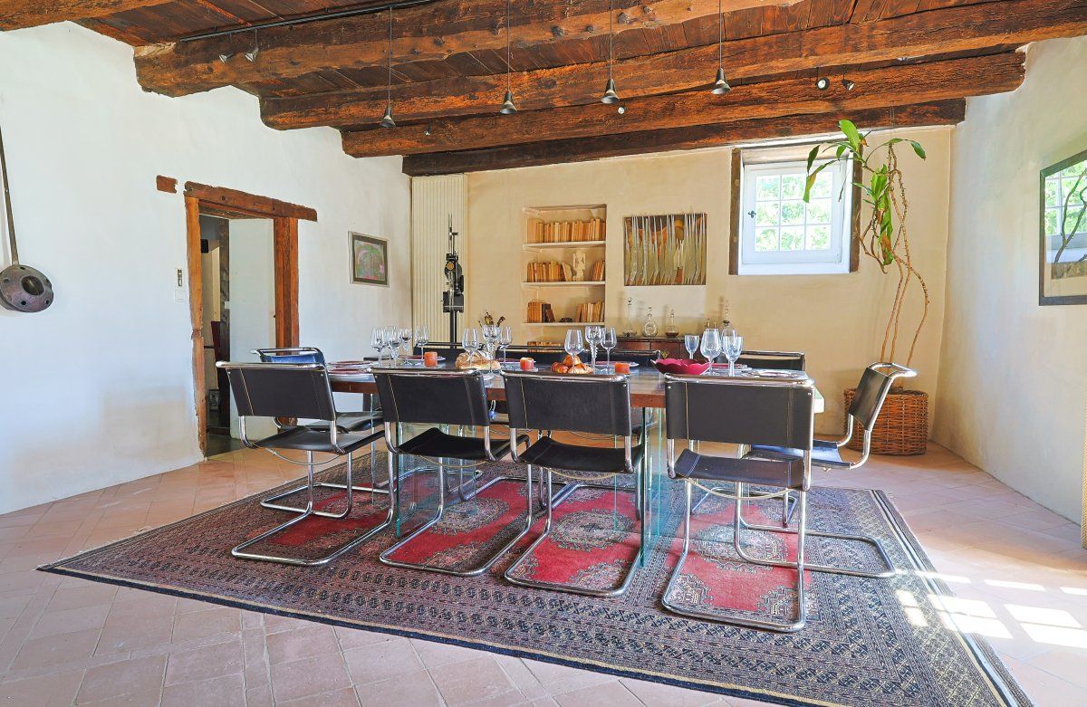 Un'area pranzo con soffitto in legno, un tappeto rosso decorato e un tavolo apparecchiato per sei persone con sedie.