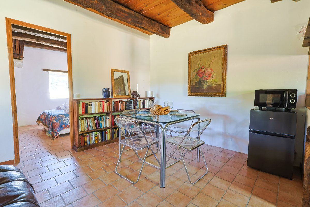 A compact living space with a kitchenette, a dining area with a glass table and chairs, a bookshelf, and a bed in the background.