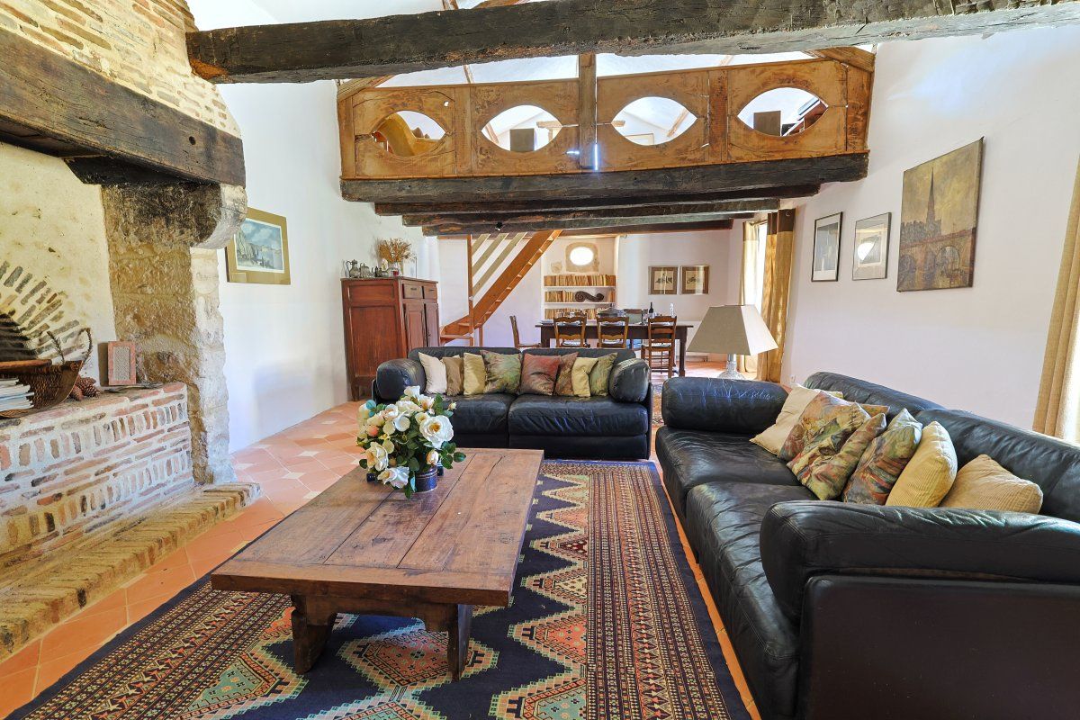 A rustic living room with exposed brick walls, a wooden ceiling, a black leather sofa, a wooden coffee table, and a patterned rug.