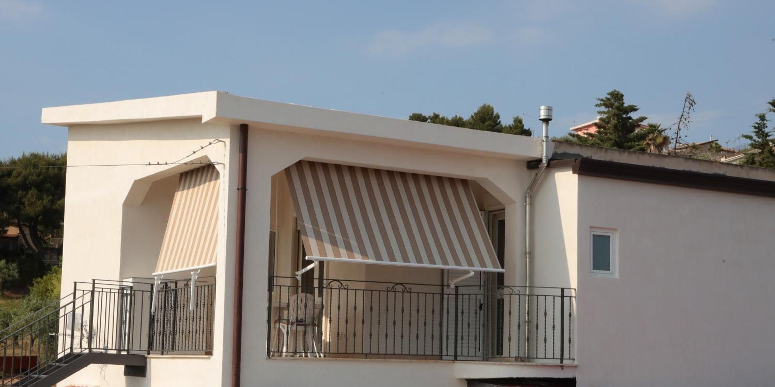Een modern gebouw met een balkon, een gestreepte luifel en een klein raam.
