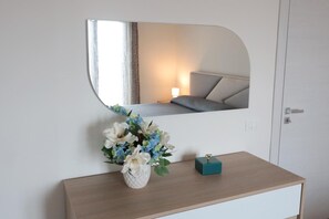 Una stanza con un letto, un comodino con un vaso di fiori e uno specchio che riflette l'ambiente.