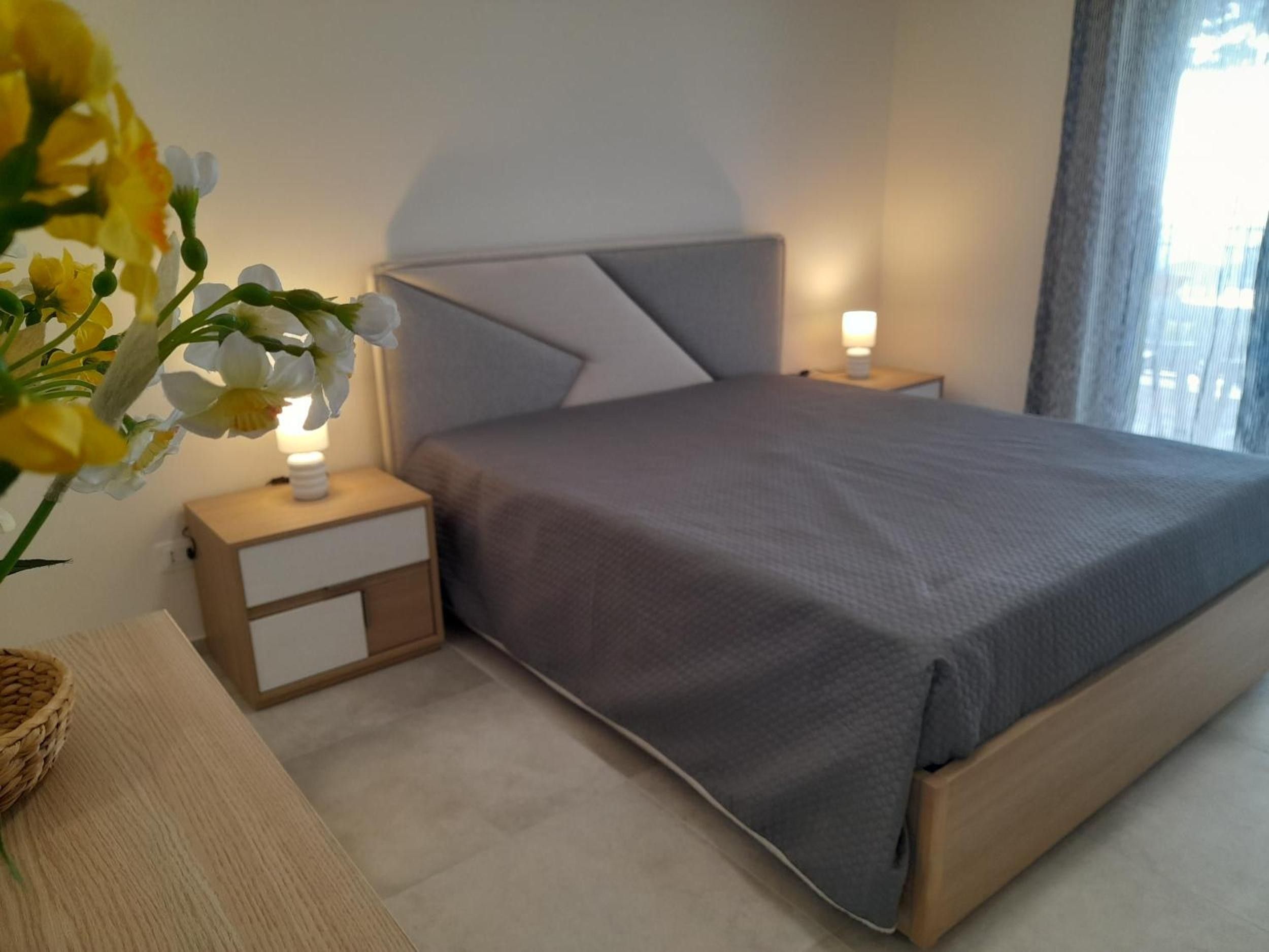 Una camera da letto con un letto, comodini, una lampada e un vaso con fiori.
