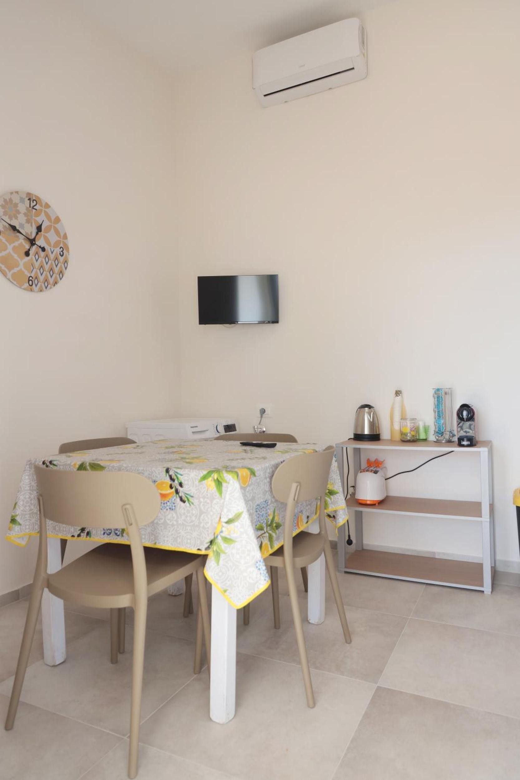 Un'area pranzo con tavolo, sedie, condizionatore d'aria, orologio e televisore a parete.