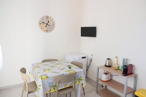 Une petite pièce propre, avec une table à manger, des chaises, une horloge, un lave-linge et une petite étagère contenant divers objets.
