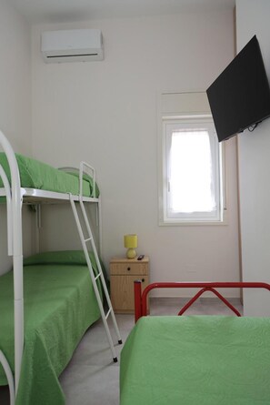 Une chambre de dortoir avec des lits superposés, une petite table de chevet avec une lampe, un téléviseur fixé au mur et une fenêtre.