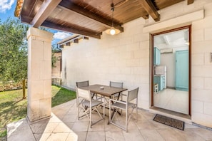 An outdoor patio with a table and chairs, a ceiling fan, and a view into a kitchen.