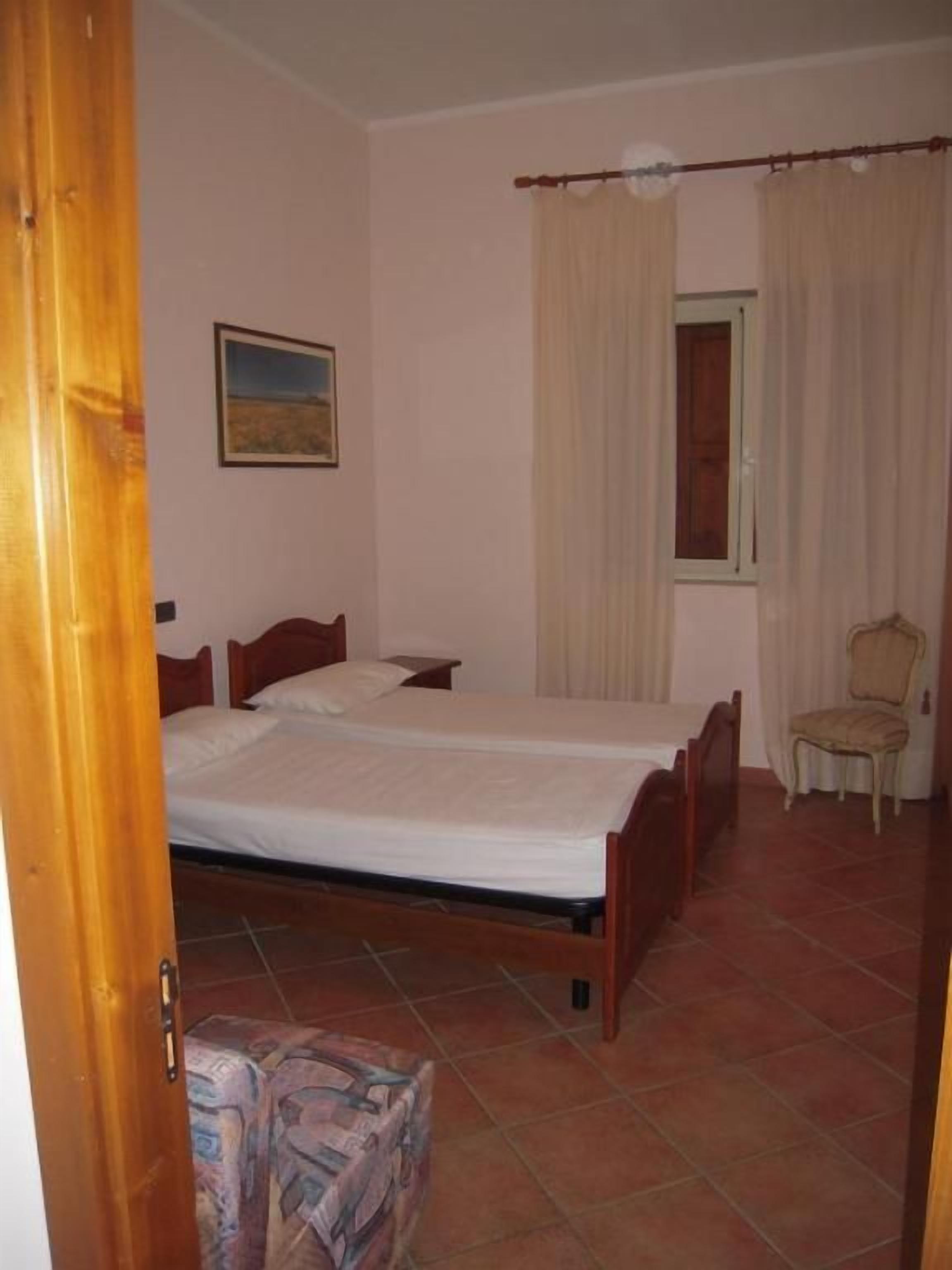 Une chambre avec deux lits, une chaise, une fenêtre avec des rideaux et une porte.