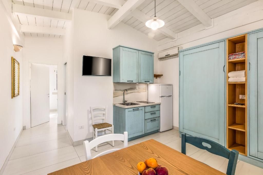 Une cuisine moderne avec des meubles bleu clair, une table à manger blanche ornée de fruits et un téléviseur fixé au mur.