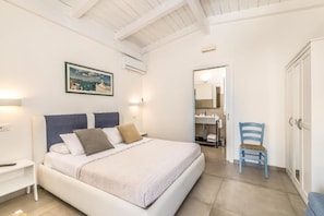 A bedroom with a bed, bedside table, chair, and a bathroom visible through an open door.