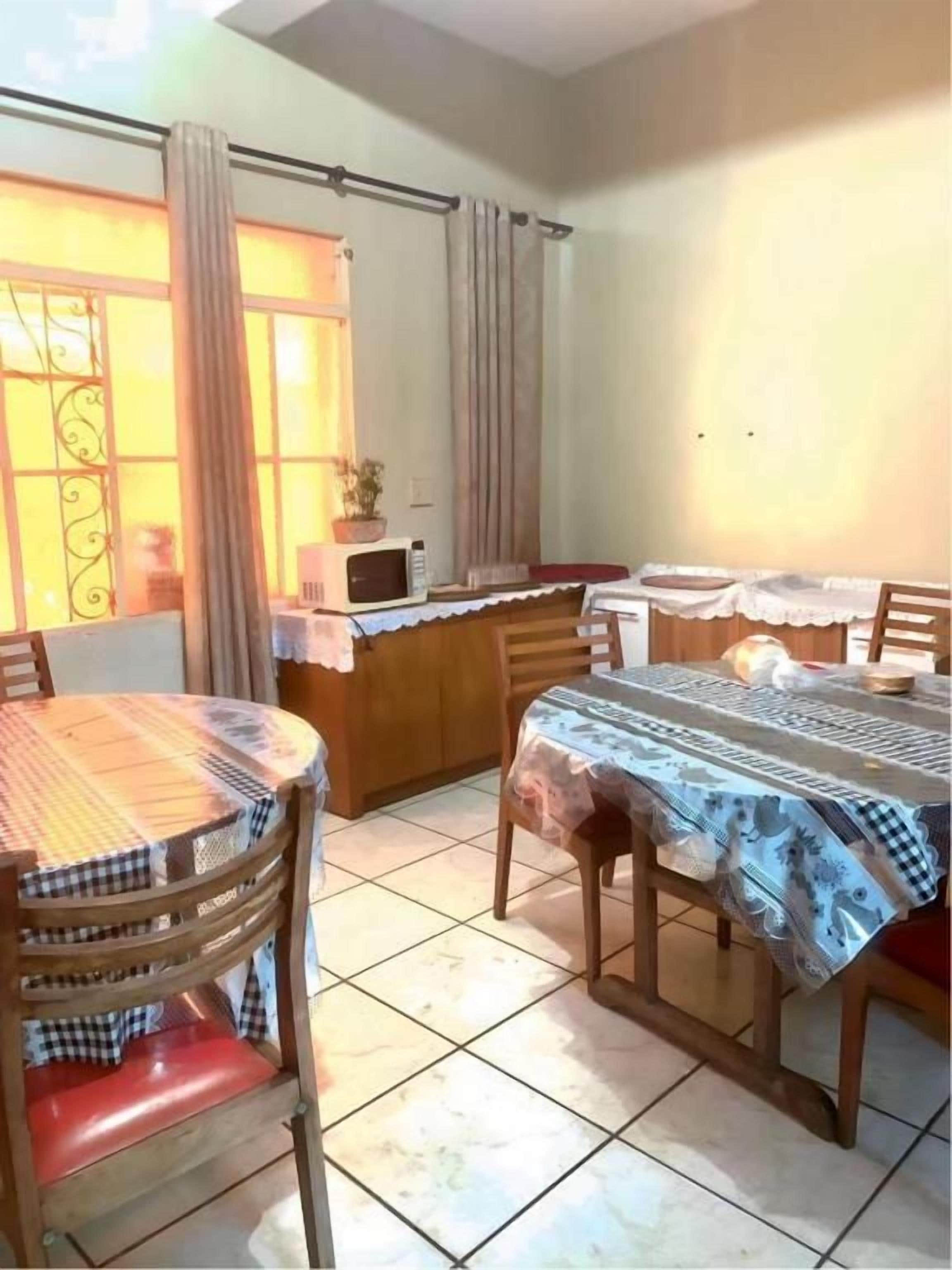 A dining area with a table and chairs, a microwave, and a window with curtains.