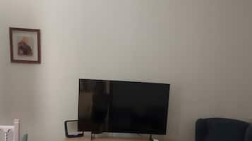 Una sala de estar con un televisor sobre un mueble de madera, un sofá azul y un suelo con baldosas rojas.