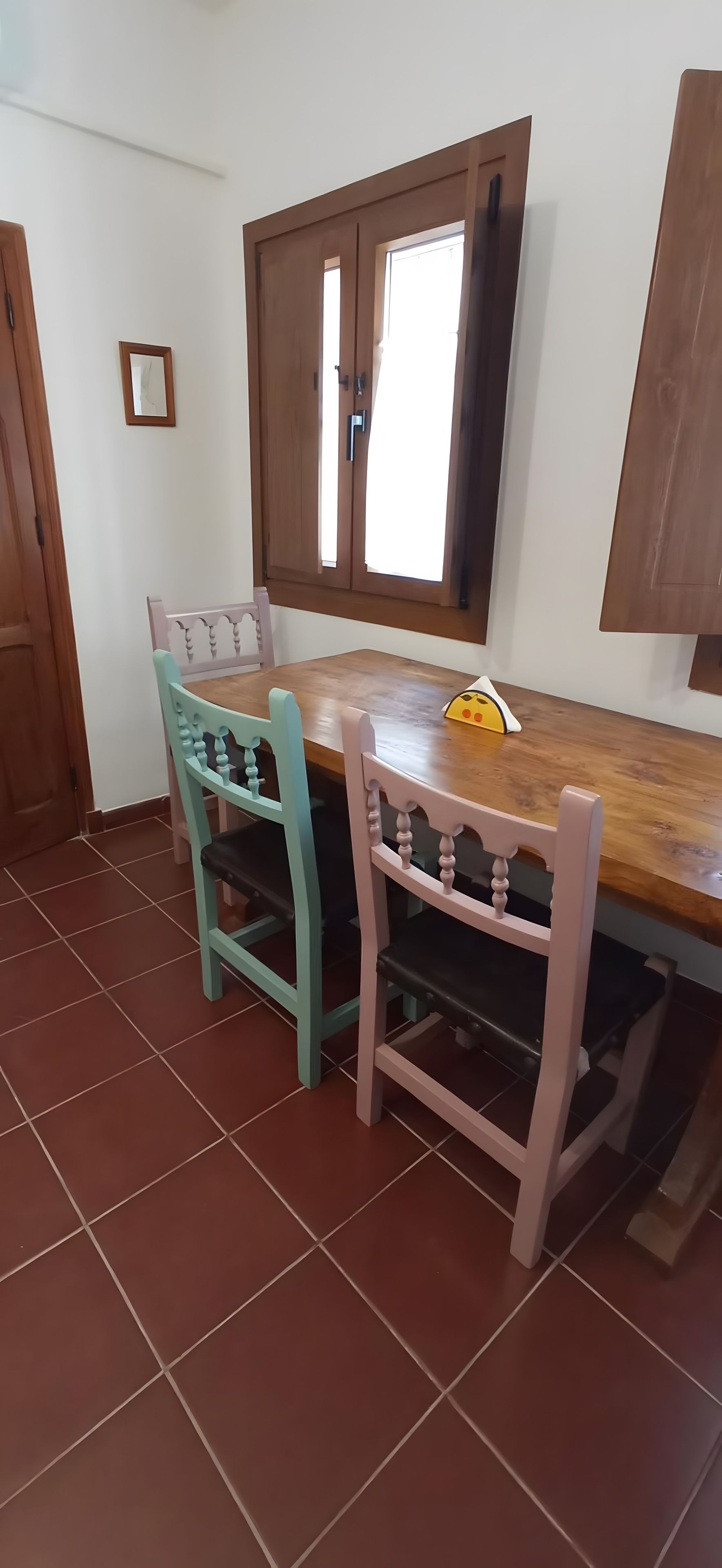Een eethoek met een houten tafel, twee stoelen, een raam met uitzicht en een deur.