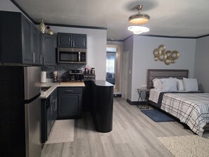 A compact kitchen with a microwave, coffee maker, and a small island. There is a bed with a headboard and pillows, and a wall-mounted light fixture. - Tranquil 1-bedroom apartment with AC in Orlando (Orlando)