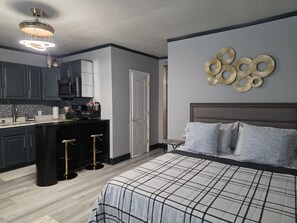 A modern bedroom with a large bed, a kitchen area with dark cabinets, and a decorative wall piece. - Tranquil 1-bedroom apartment with AC in Orlando (Orlando)