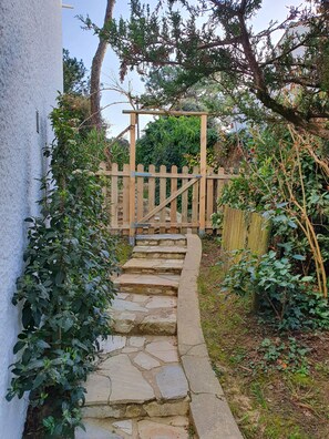 Un escalier en pierre mène à une porte en bois, qui est elle-même entourée de verdure et d’un mur blanc.