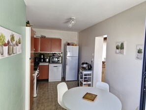 Une cuisine compacte équipée d’un réfrigérateur, d’un four à micro-ondes et d’une cuisinière. On y trouve une table à manger avec des chaises, et une petite plante en pot posée sur la table.