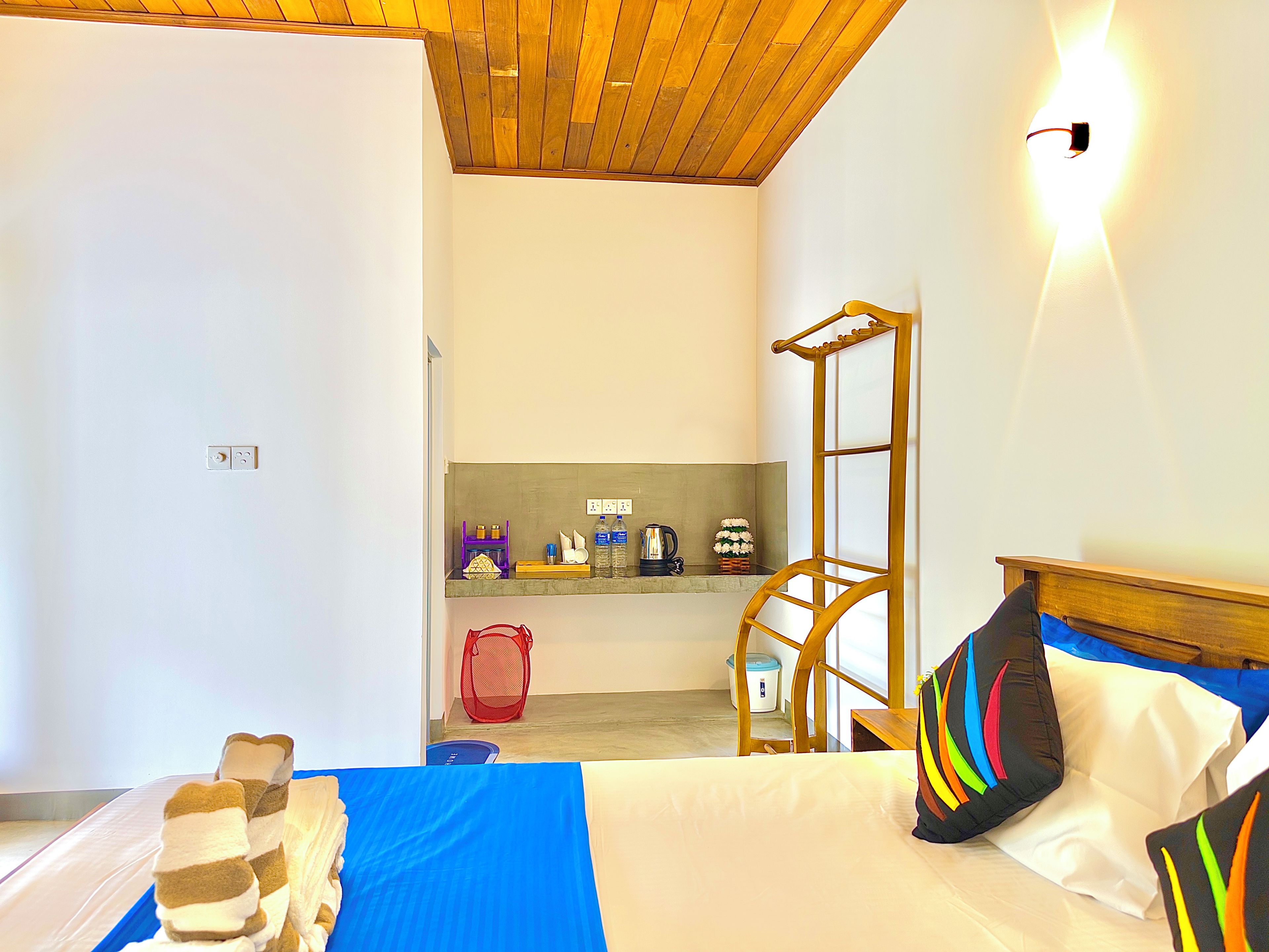 A hotel room with a bed, a wooden ceiling, a small kitchenette, and a bathroom.