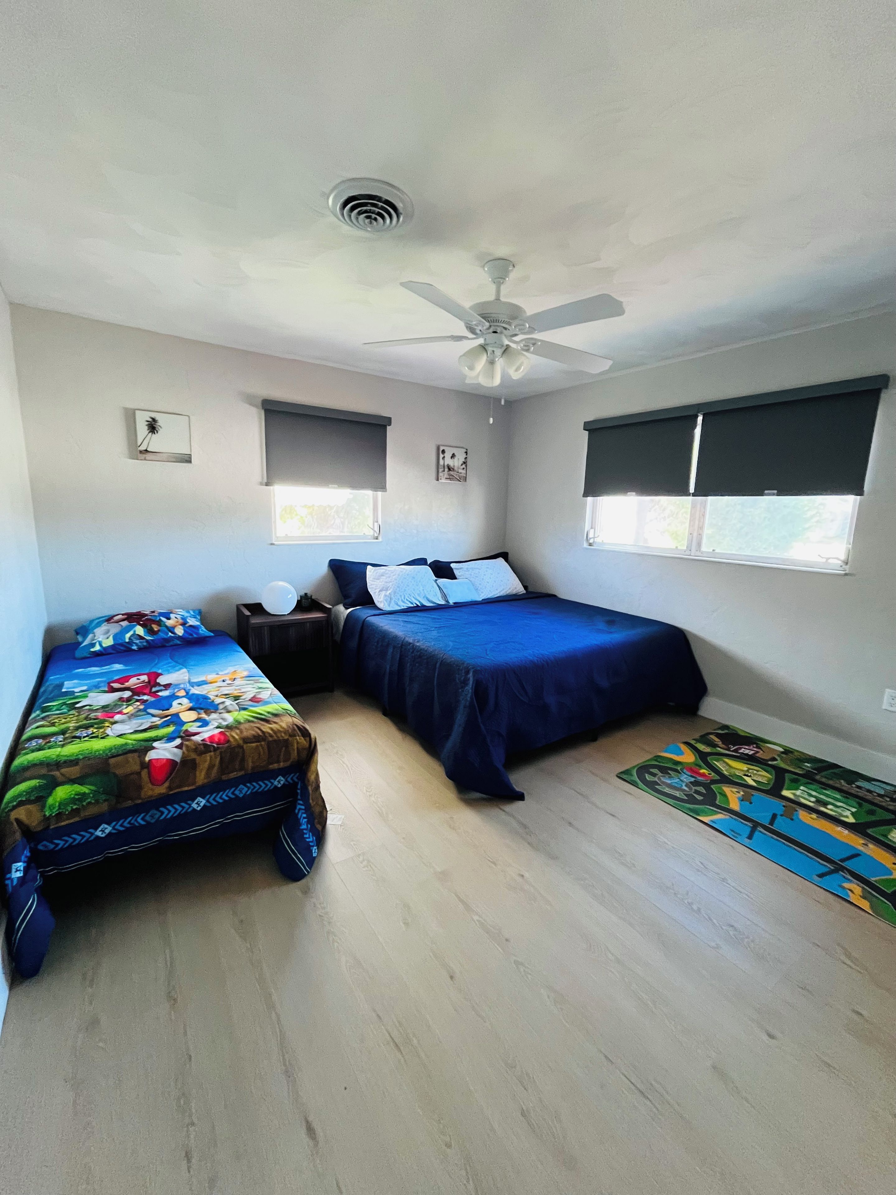 Ein Schlafzimmer mit zwei Betten, einem Deckenventilator und einem Fenster mit Jalousien.