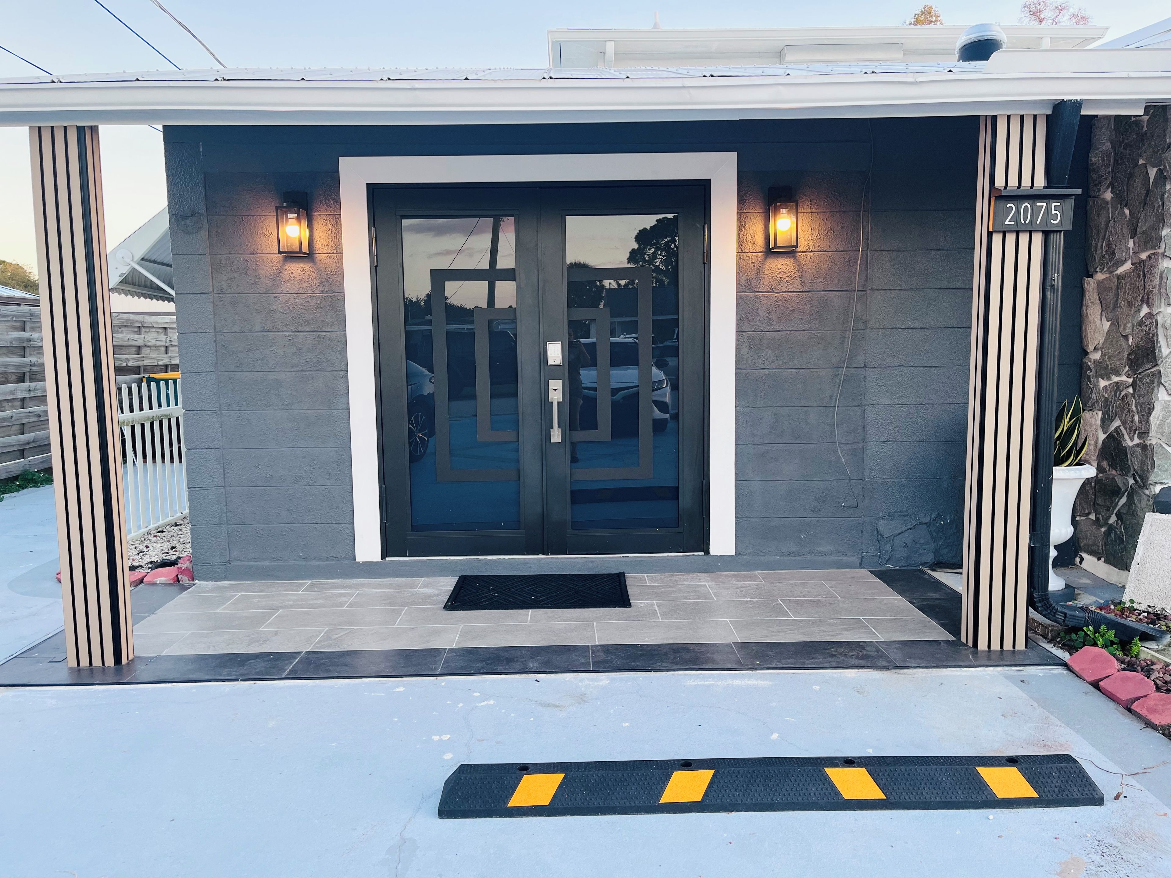 A modern building entrance with a glass door, a number sign, and a small garden area.