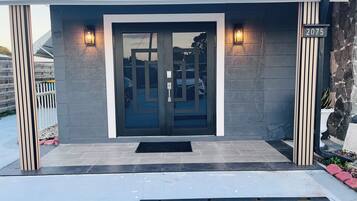 A modern building entrance with a glass door, a number sign, and a small garden area.